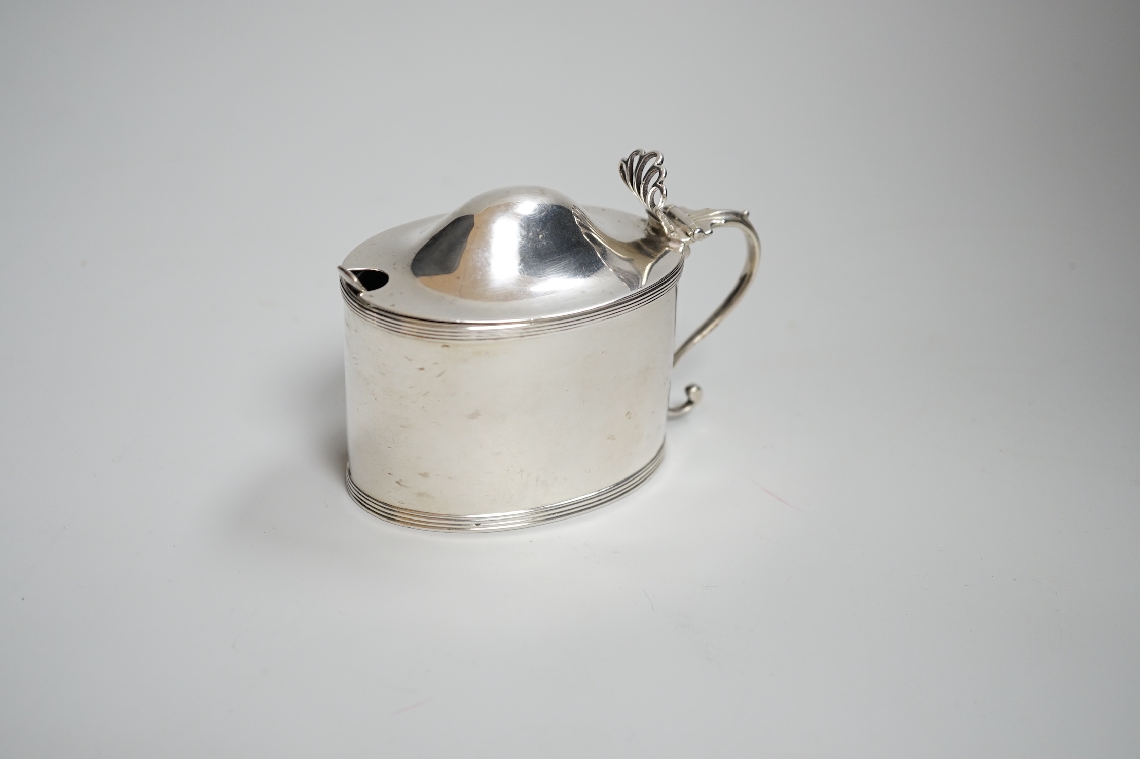 A George III oval silver drum mustard, with domed lid, blue glass liner and associated plated spoon, makers Peter, Anne and William Bateman, London 1799, 110 grams